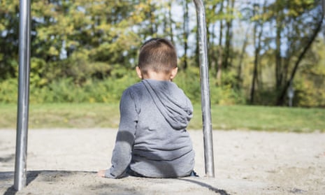 A young boy sits with his back to camera, alone on a playground roundabout
