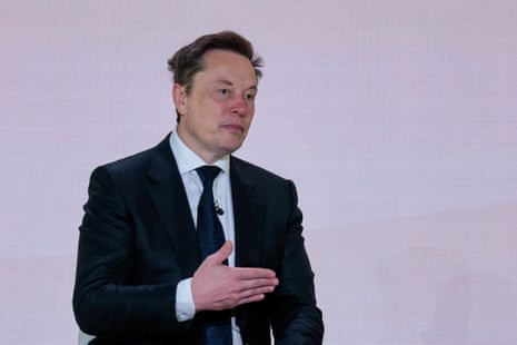 Elon Musk, in a dark suit and tie, gestures with his hands while speaking