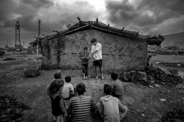 A small group of children sitting in the dirt attend an open-air class