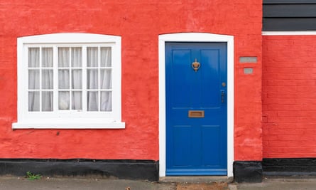 A brightly colored cottage in a British village with red walls and a blue door.