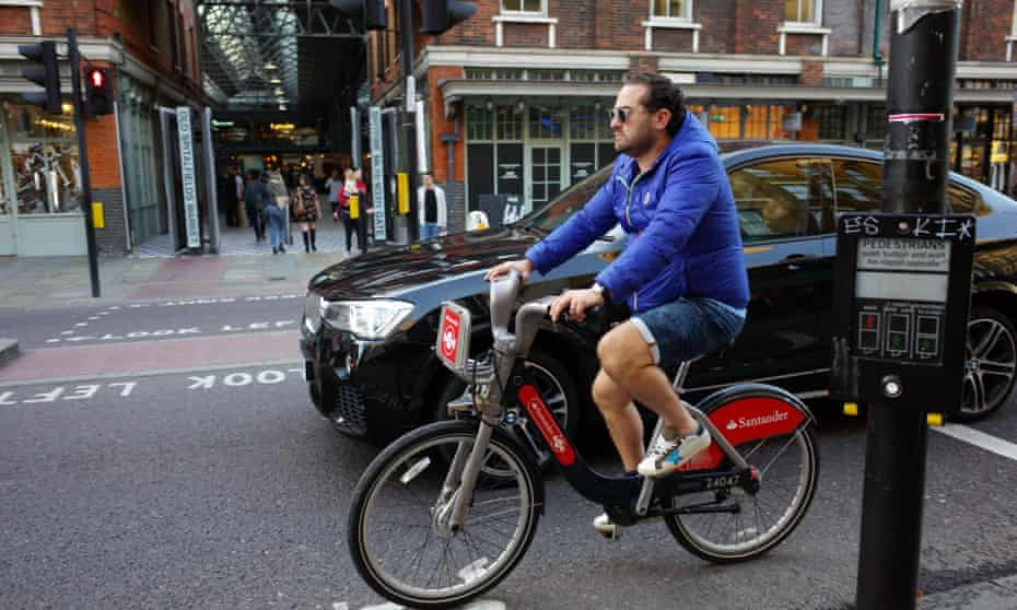 Cyclist riding hire bike alongside BMW car in Shoreditch, London