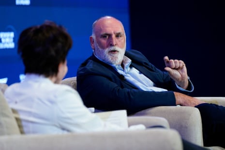 a man in a suit speaks to a woman while seated on stage
