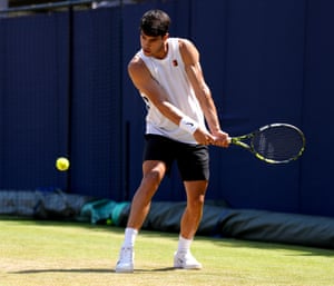 A man in a white vest and black shorts about to play a backhand shot on a grass tennis court