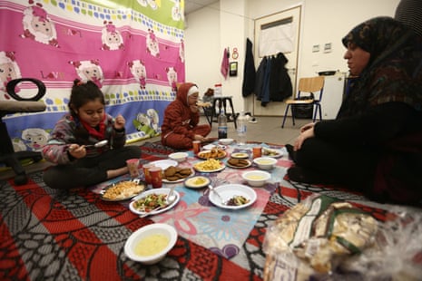 a woman eats a meal with her two children on the floor of a classroom