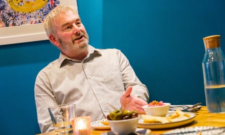 A man sitting talking at a restaurant table in front of a blue wall