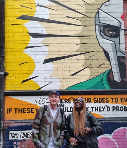 a man and a woman smiling in front of a mural of a man in a Dr Doom mask