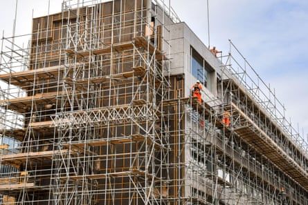 Construction workers standing on scaffolding high above a street in central London.