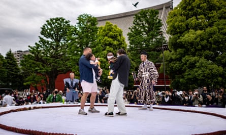 Two babies in their parents arms in a sumo ring as part of a crying baby competition.