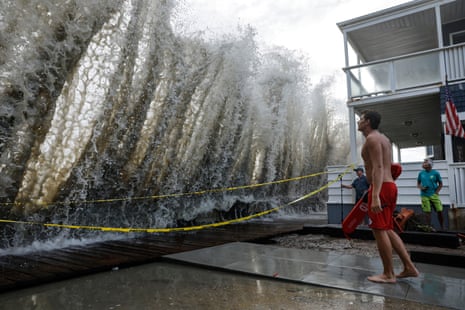 A lifeguard watches a huge wave crash over a seawall by a closed boardwalk
