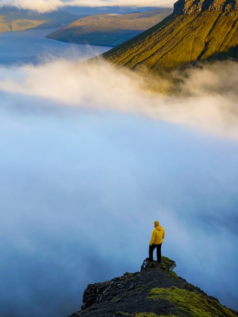 Man on mountain rock looking down on clouds and sunrise