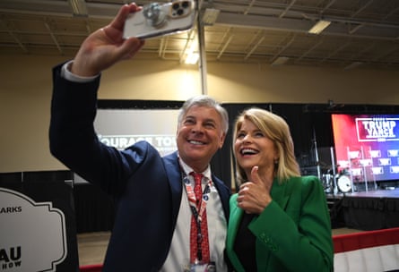 A man holds up a camera to take a selfie with a woman, who is giving a thumbs up and smiling.