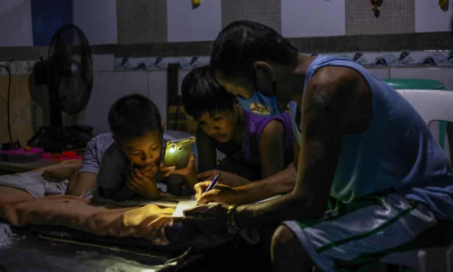 Petronilo Pacayra signe des documents scolaires avec ses enfants âgés de neuf et 10 ans, à Quezon City.