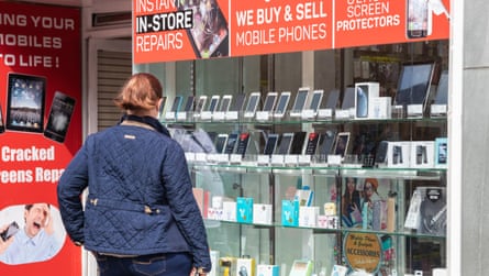 A woman looks at the mobile phones displayed in a shop window.