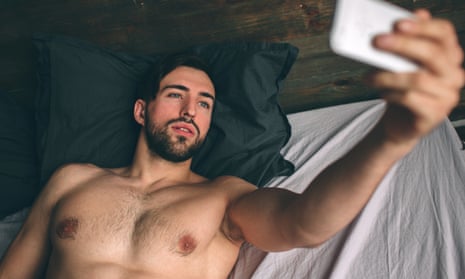 Shirtless, bearded, dark-haired man taking a selfie in bed