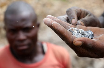 A hand with coltan in it, with a blurred man’s face in the background.