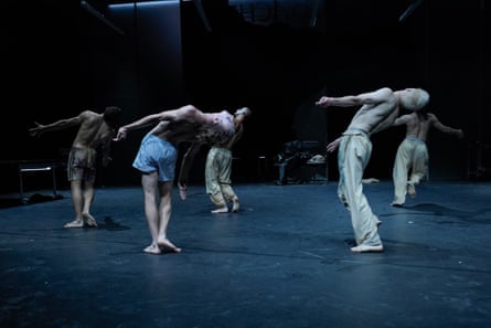 Shirtless dancers lean back as they perform on a dimly lit stage.