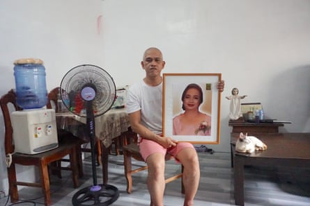 A man sits on a chair holding a large framed photograph of a woman.