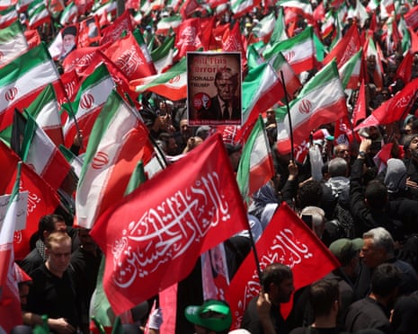 A poster of Trump reading 'Kill this terrorist' is surrounded by Iranian flags during a funeral procession.