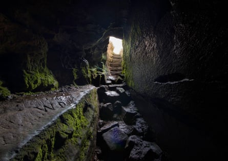 A mossy stone passage leads to steps rising towards daylight