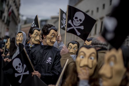 People wearing caricature masks of Salvador Dalí carry skull and crossbones flags through a street