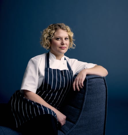 A female chef with blond hair in a white shirt with a blue and white apron