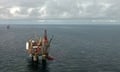 Aerial view of the Gullfaks C oil platform in the North Sea: it is seen as a small construction with cranes and drilling rigs in an expanse of smooth but dark grey sea which stretches to the horizon; the sky is also grey, and cloudy