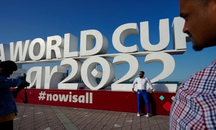 A man poses in front of a sign that says he has been photographed for the 2022 World Cup in Qatar 