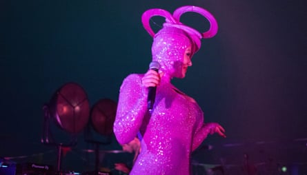 DJ Tanzer performing in a bright pink catsuit with an elaborate headdress.