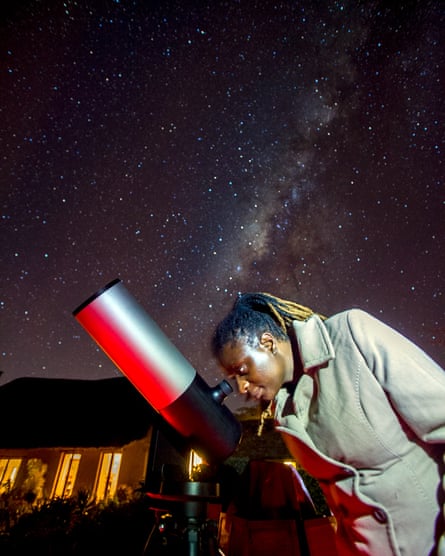 An African woman looks through a telescope against a backdrop of a starry night sky