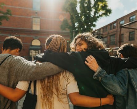 Smiling young man looking over shoulder while walking with arm around friends at street on sunny day