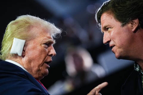 Two men, one with a shock of long blond hair and a bandage on his ear, speak with each other