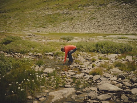 A man stoops to pick something out of a mountain stream