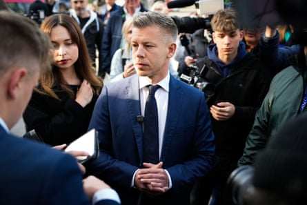A man in a dark suit talking to journalists