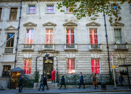People walk past Annabel’s in Mayfair, which looks like a luxurious town house with a doorman wearing red on the door