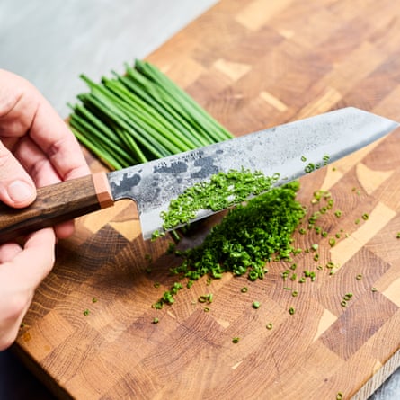 A knife and chopped chives on a wooden board