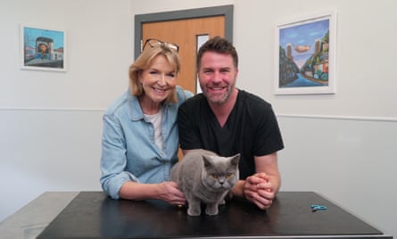 A woman and man in a vet surgery leaning on a table with a grey cat