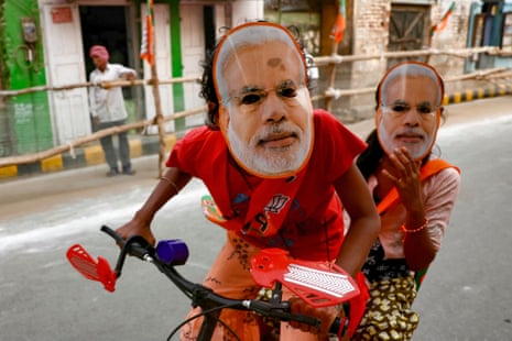 Children wearing Narendra Modi masks ride a bicycle in Varanasi