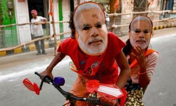 Children wearing Narendra Modi masks ride a bicycle in Varanasi
