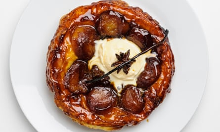 A round white plate with a caramelised round flaky pastry tart with apple halves and a scoop of vanilla ice-cream in the middle