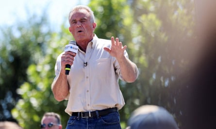 a man in shirtsleeves speaks into a microphone outdoors