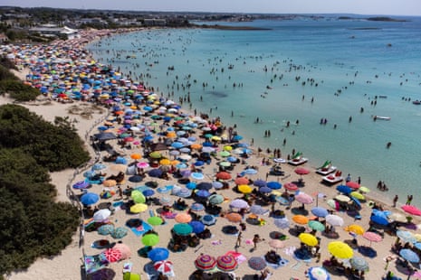 Aerial view of densely packed beach umbrellas on a crowded sandy beach with clear blue water