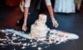 A wedding cake is dropped on the floor as two hands covered in frosting try to clean it up.