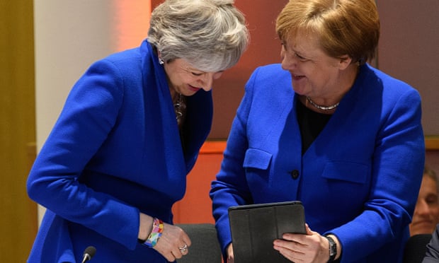 Theresa May and Angela Merkel in royal blue jackets looking at an iPad
