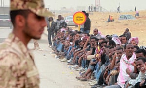 A Saudi police officer stands next to undocumented foreign workers in Riyadh, Saudi Arabia.