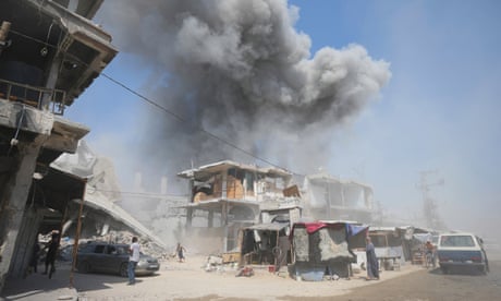 A boy runs away as smoke rises from behind buildings, while a few other people turn to look