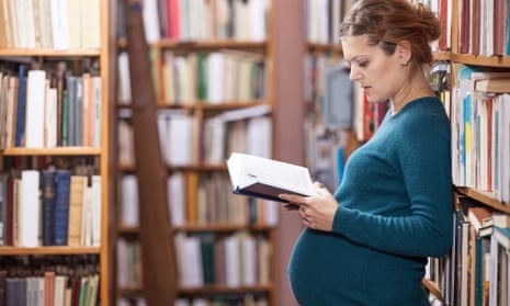 Young pregnant woman reading book in library