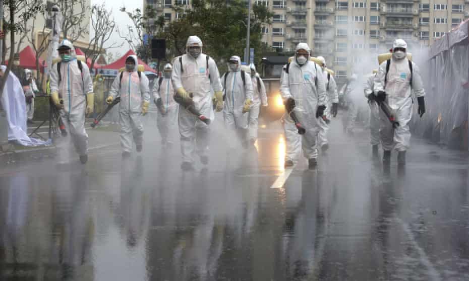 Taiwanese army soldiers wearing protective suits spray disinfectant over a road in New Taipai City.