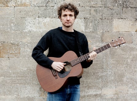 Sam Amidon in a black jumper with a guitar.