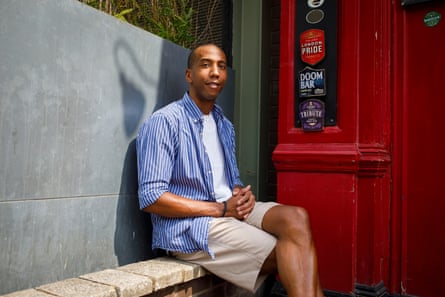 a man in shorts and a striped top sits on a bench next to a red door