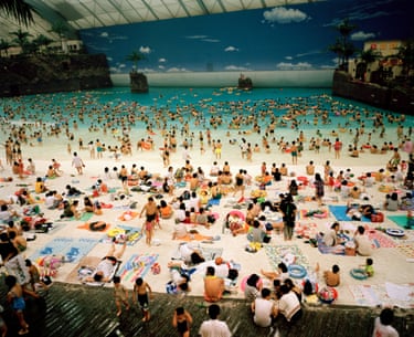 A crowded indoor artificial beach at Ocean Dome, people sunbathing and swimming under a painted sky